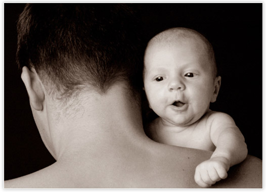 Schwarzweißfoto- Vater mit Neugeborenen über Schulter schauend